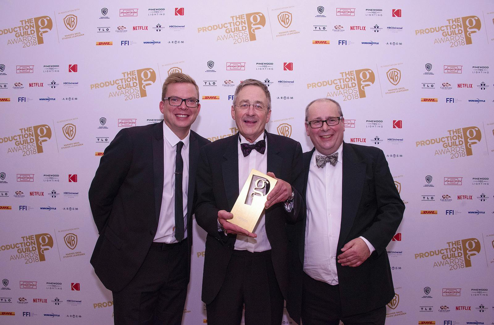 Gareth Tandy standing in a suit with two other men, holding his award